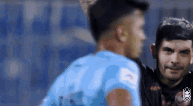 a man in a blue shirt is talking to another man in a black shirt .