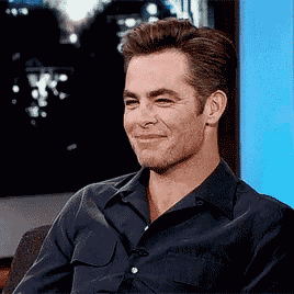 a man in a black shirt is smiling while sitting in front of a blue wall
