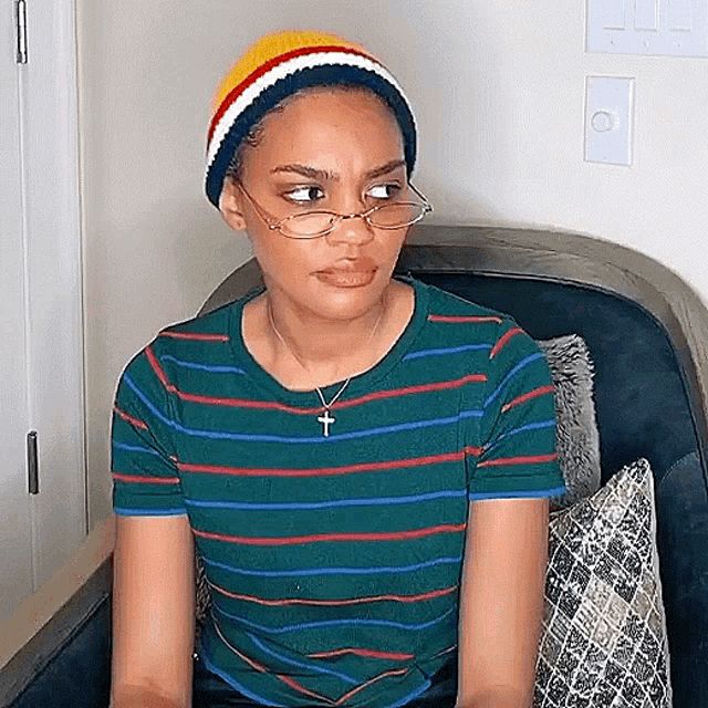 a woman wearing glasses and a beanie is sitting on a couch .