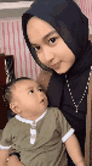 a woman in a hijab is holding a baby .