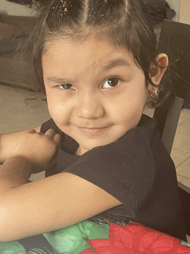 a little girl in a black shirt sits at a table and smiles