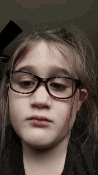 a young girl wearing glasses looks down at something