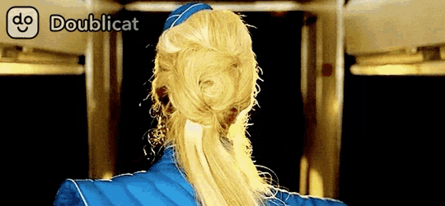 a woman with blonde hair is wearing a blue jacket and a blue hat with doublicat written above her