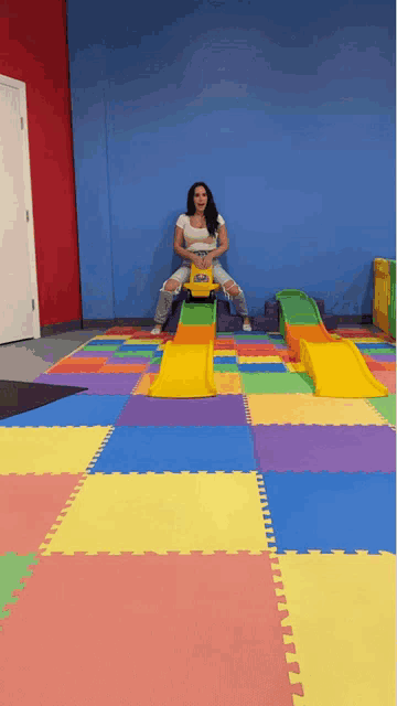 a woman rides a toy car on a colorful mat