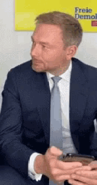 a man in a suit and tie is sitting in front of a yellow sign that says freie demokrate