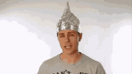 a man wearing a tin foil hat and a gray shirt is making a face .