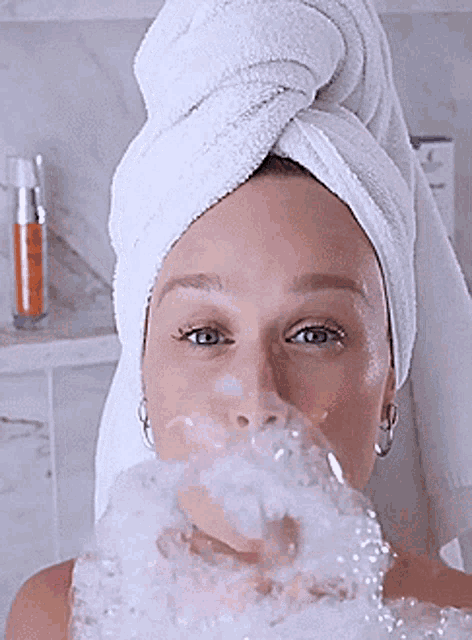 a woman with a towel wrapped around her head is blowing bubbles out of her mouth