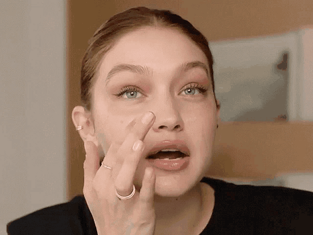 a woman with a ring on her finger applying cream to her face