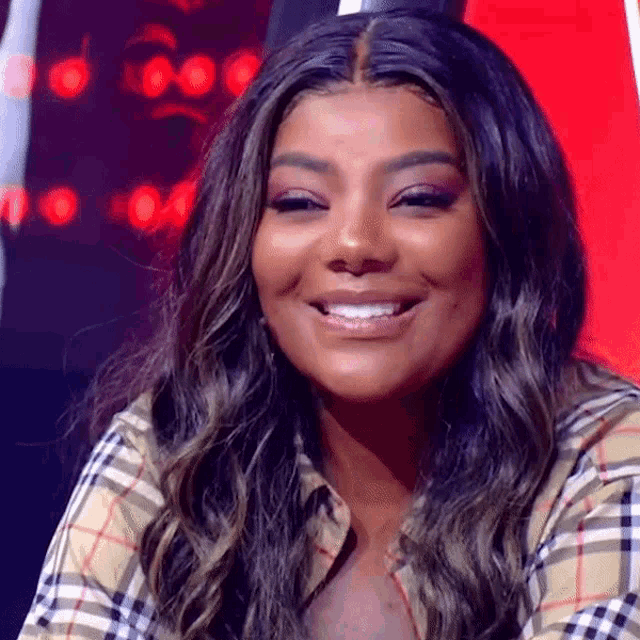 a woman wearing a plaid shirt is smiling while sitting in front of a microphone .