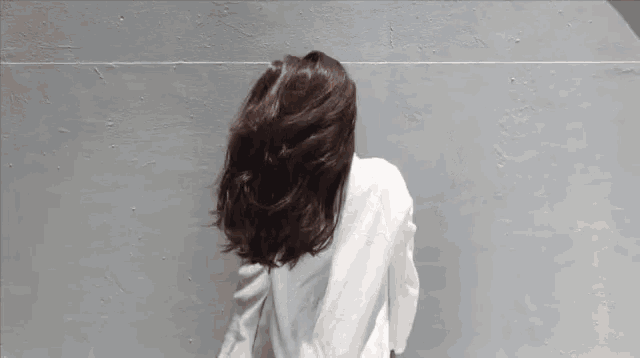 a woman in a white jacket stands in front of a wall with the words que diiiste