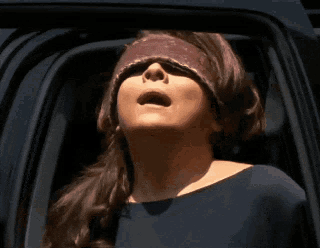 a woman wearing a blindfold looks up at the sun