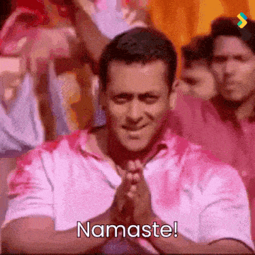 a man in a pink shirt says namaste with his hands folded