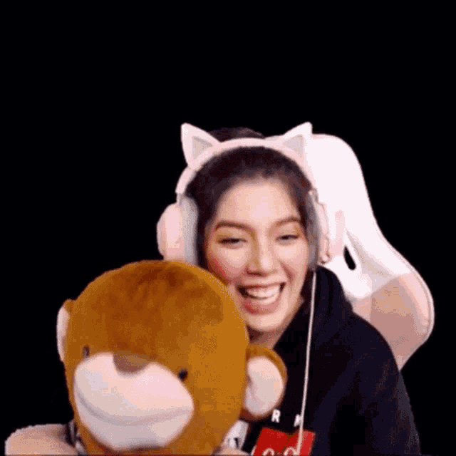 a woman wearing cat ears is holding a teddy bear and smiling .