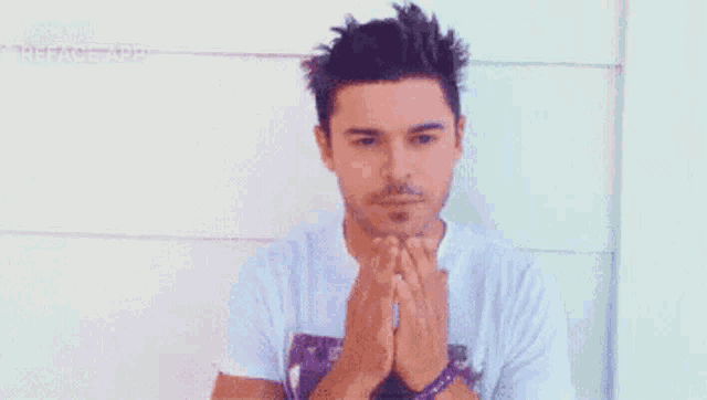a man in a white shirt holds his hands together in front of a white wall