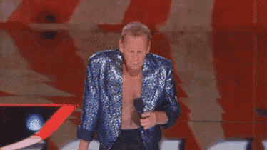 a man in a blue jacket is standing on a stage without a shirt on .