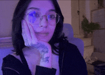 a woman with glasses and a tattoo on her hand is sitting in a chair .