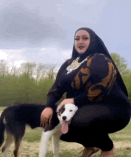 a woman in a hijab is kneeling down with a dog on her lap