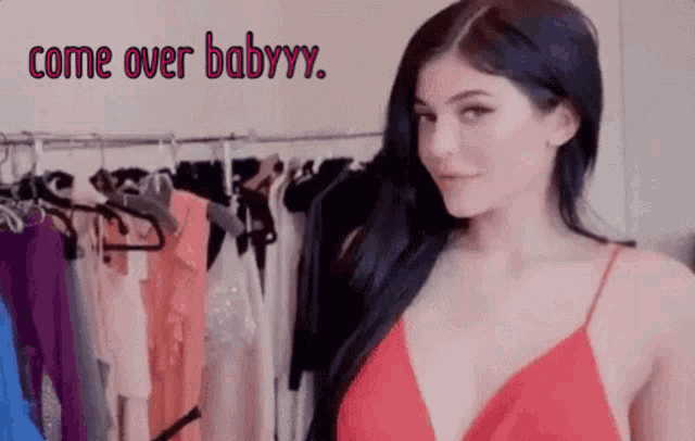 a woman in a red dress is standing in front of a rack of clothes with the words `` come over babyyy '' .