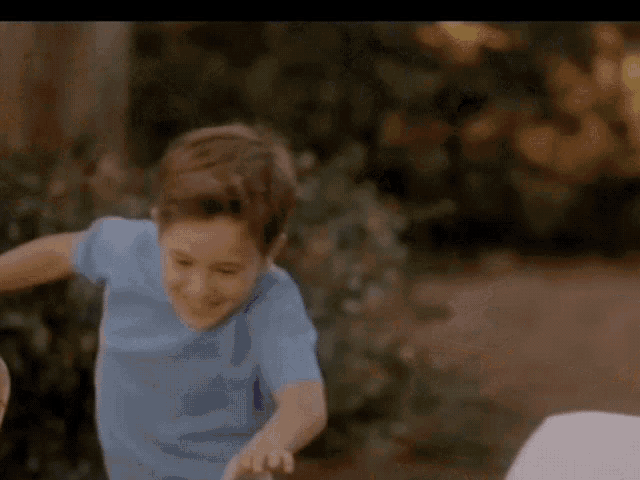 a young boy wearing a blue shirt and a baseball cap is running in a park .
