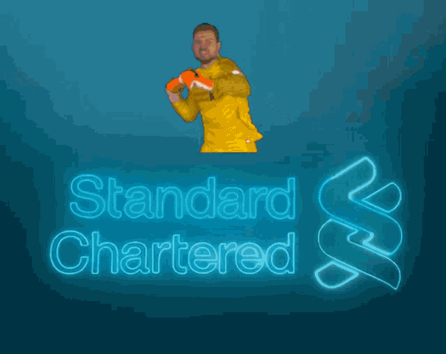 a man in a yellow shirt holds up his fist in front of a neon sign that says standard chartered