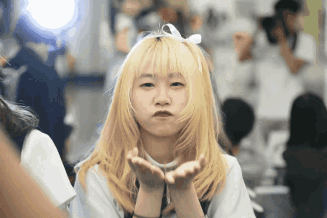a girl with blonde hair is blowing a kiss at the camera
