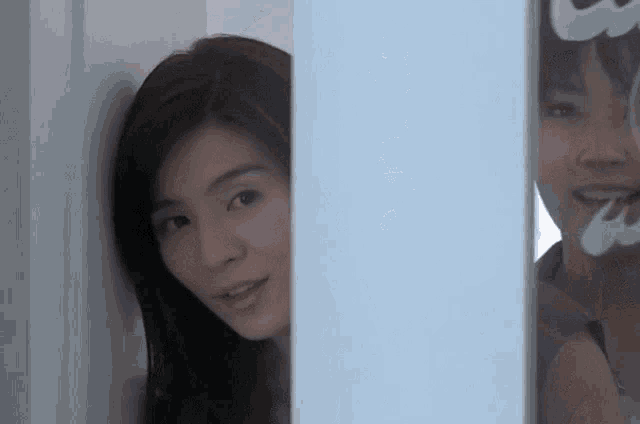 a woman peeking out from behind a glass door with a reflection of herself in it