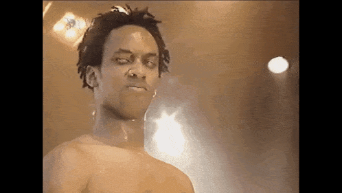 a shirtless man with dreadlocks and a nose ring is standing in front of a stage .