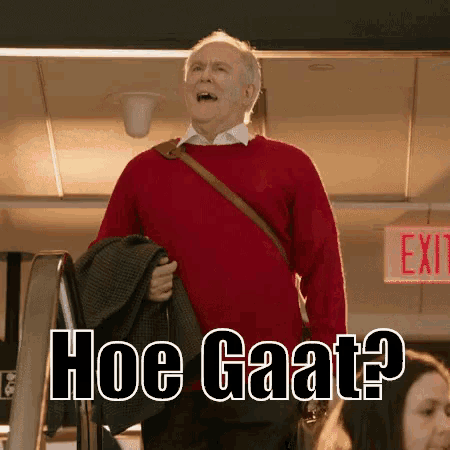 an older man in a red sweater is standing in front of a red exit sign