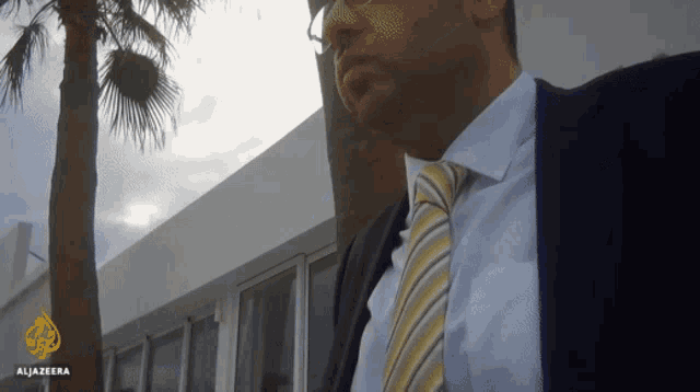 a man in a suit and tie is standing in front of a building that says alijazeera on the bottom
