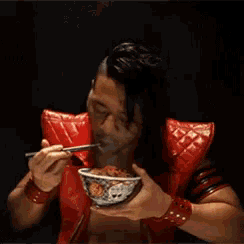 a man in a red jacket is holding a bowl of food in his hands .