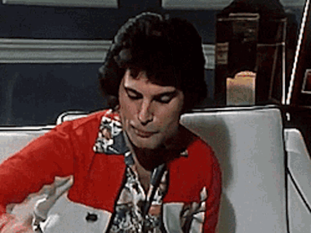 a man in a red jacket and floral shirt is sitting on a white couch .