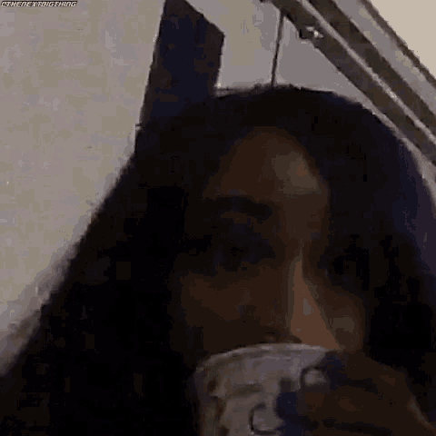 a woman with purple hair is drinking from a cup in a dark room .