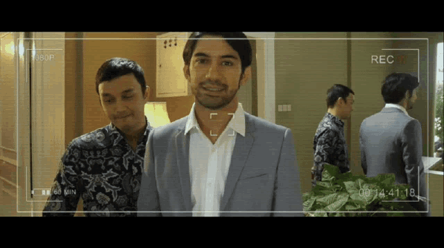 a man in a suit and a man in a floral shirt are being recorded on a camera