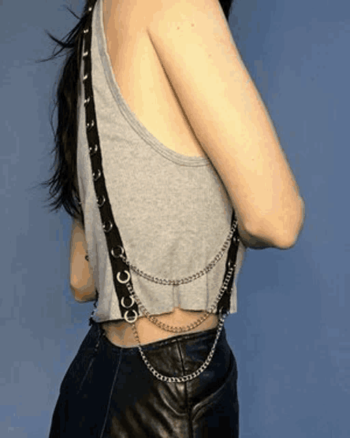 a woman is wearing a gray tank top with a black strap and chains .