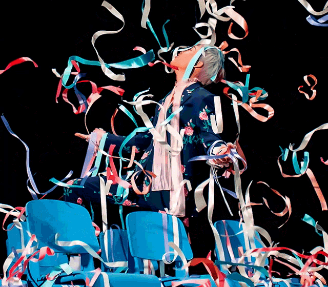 a woman in a blue jacket is surrounded by blue chairs and ribbons