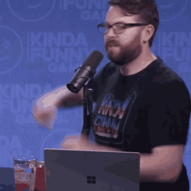 a man wearing a kinda funny shirt stands in front of a microphone and a laptop