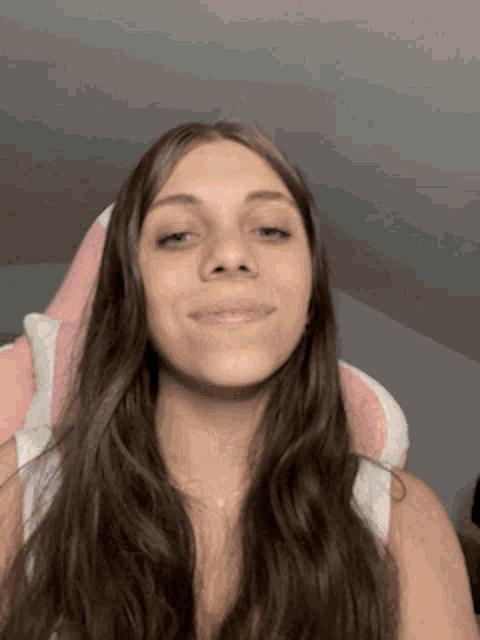 a woman with long brown hair is sitting in a pink and white chair .