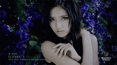 a woman in a black dress is surrounded by purple flowers and the words still flower on the bottom