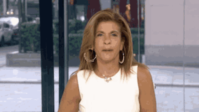 a woman wearing a white top and hoop earrings looks at the camera