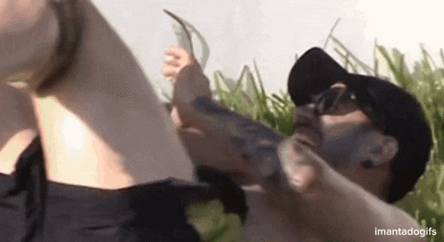 a man is licking a woman 's feet in a field while wearing a hat and sunglasses .
