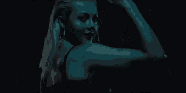 a woman in a black bra is dancing in a dark room with her arms outstretched .