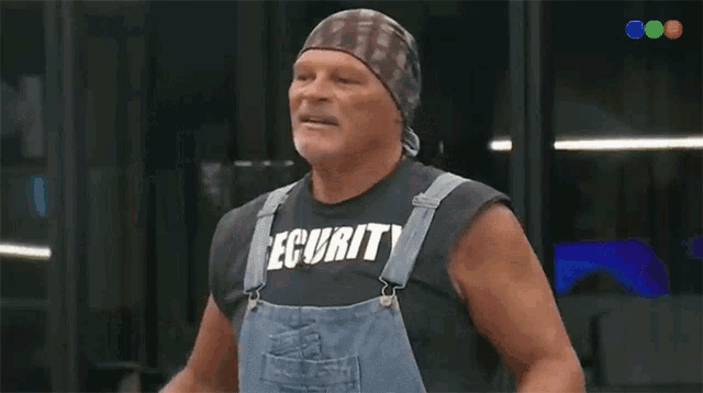 a man wearing overalls and a shirt that says curly is giving a thumbs up