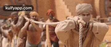 a man in a turban is holding a rope in his hands in front of a group of men .