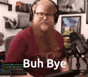 a man with a beard wearing headphones and glasses is sitting in front of a microphone and says buh bye