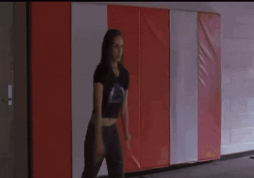 a woman in a black crop top is jumping in front of a red white and blue wall