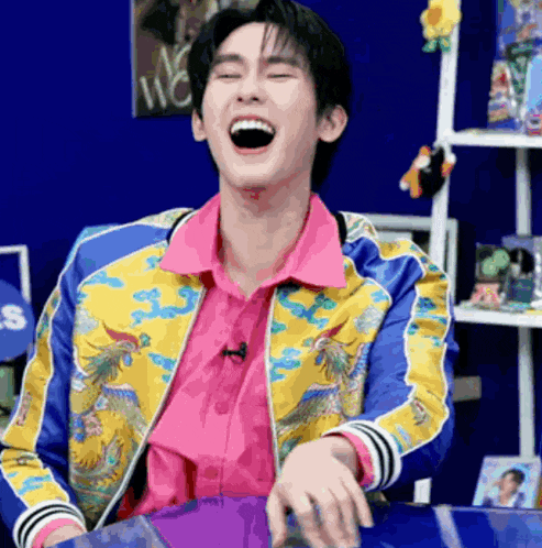 a man wearing a colorful jacket is laughing with his mouth open .