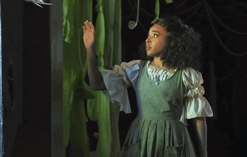 a girl in a green dress is reaching out towards a claw