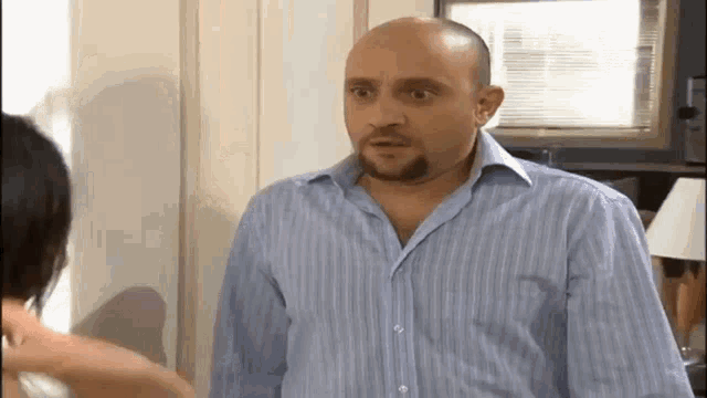 a bald man with a beard is talking to a woman in a blue striped shirt .