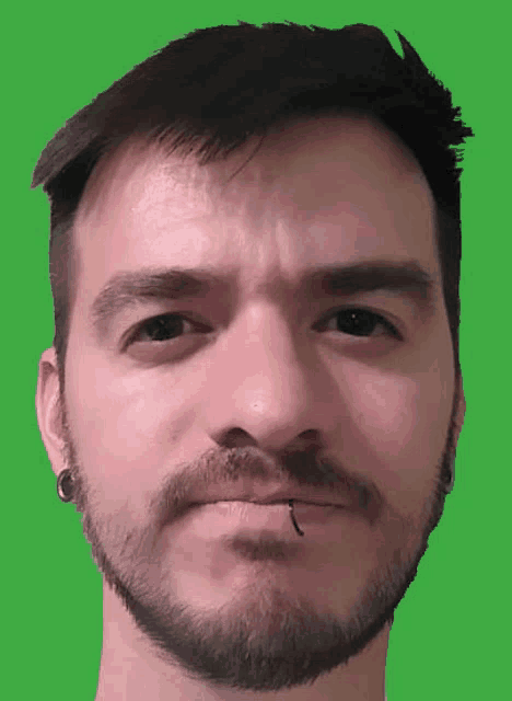 a man with a beard and ear piercings looks at the camera
