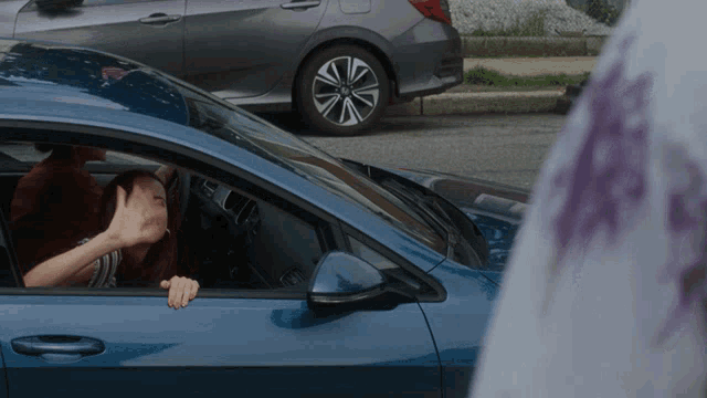 a woman is sitting in a blue car covering her face